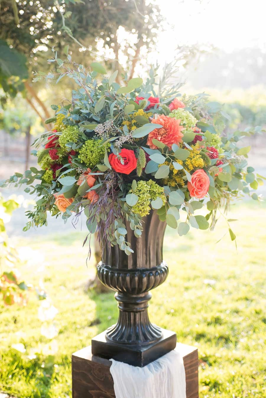 Coral rose and eucalyptus urn arrangement in a sunlit vineyard